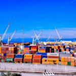 A bustling shipping port with colorful stacked containers and numerous cranes under a clear blue sky.